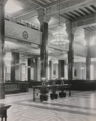 A black-and-white photograph of the interior of an ornate office lobby with inlaid floors, columns, and chandeliers.