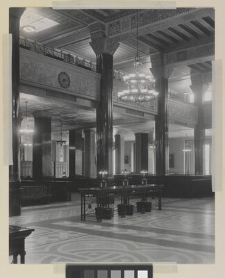 A black-and-white photograph of the interior of an ornate office lobby with inlaid floors, columns, and chandeliers.