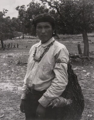 A black-and-white photograph of an Indigenous man carrying a large bag.