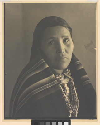 A black-and-white portrait photograph of an Indigenous woman with a blanket wrapped around her neck and shoulders.