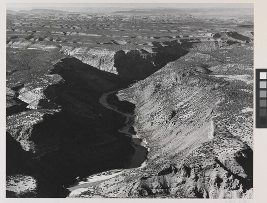 A black-and-white photograph of an aerial view of a river winding through a steep canyon.
