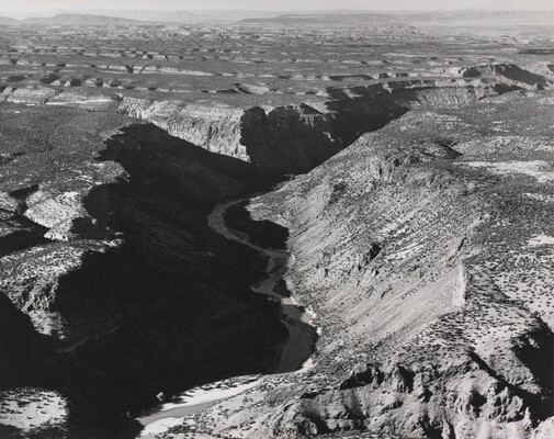 A black-and-white photograph of an aerial view of a river winding through a steep canyon.