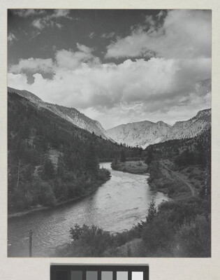 A black-and-white photograph of a river winding through a mountain valley under a cloudy sky.