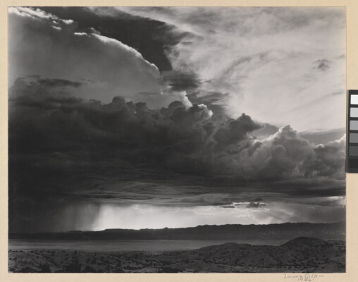 A black-and-white photograph of torrential rain and dark, heavy storm clouds passing into a brightly lit plain.