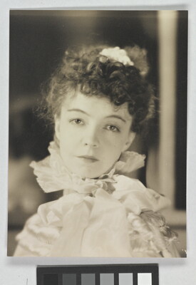 A black-and-white portrait photograph of a White woman with curly hair pulled on top of her head, wearing a top with a ruffled collar.