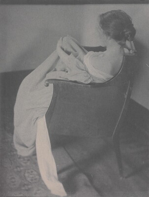 A black-and-white photograph of the back of a seated White woman wearing a long off-the-shoulder dress with her hair pulled up in a loose bun.