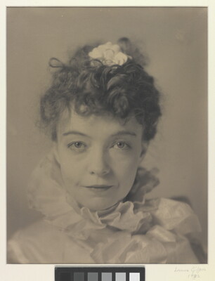 A black-and-white portrait photograph of a White woman with curly hair pulled on top of her head, wearing a top with a ruffled collar.