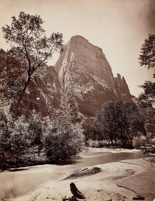 A black-and-white photograph of a shallow river with trees on the far shore and a tall rock formation in the background.