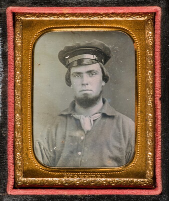 A black-and-white photograph in a gold frame and case of a young man posed in a military hat.