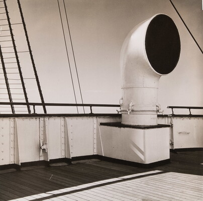 A black-and-white photograph of a large ventilation pipe coming out of the deck of a ship.