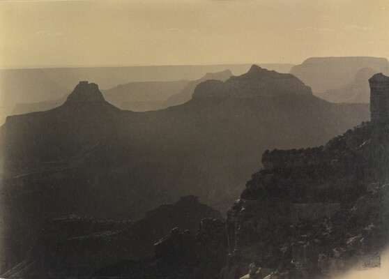 A sepia-toned photograph of the silhouettes of mesas, rock formations, and distant mountains.