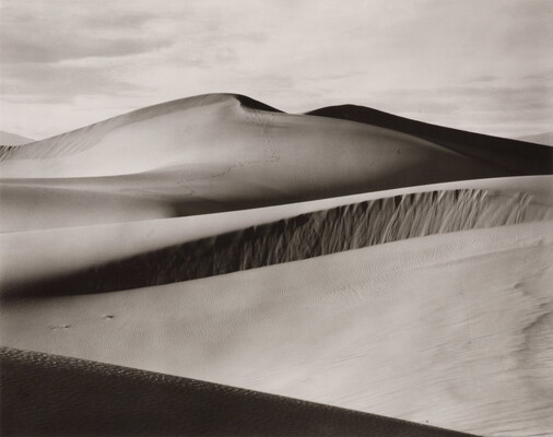 A black-and-white photograph of rolling sand dunes.