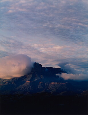 A color photograph taken from a high vantage point of mountain peaks surrounded by storm clouds.