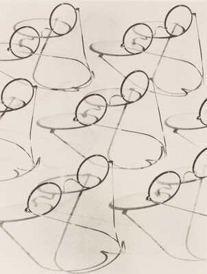 A black-and-white photograph of multiple granny-style eyeglasses and their shadows.