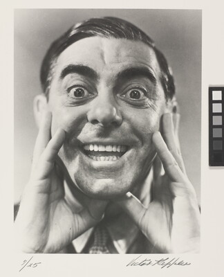 A black-and-white portrait photograph of a White man, hair slicked back, hands framing his cheeks, mouth open in a wide smile.