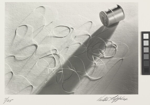 A black-and-white photograph of a spool of thread laying on its side with loose thread in loops around it.