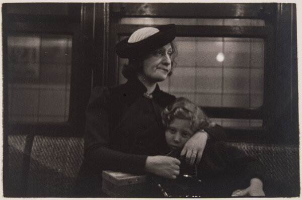 A black-and-white photograph of a White woman with her arms around a child; both seated on an upholstered seat with windows behind them.