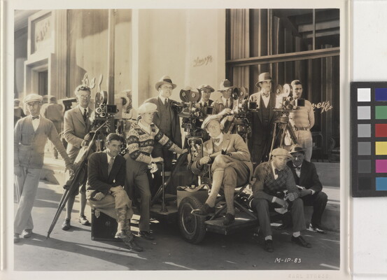 A black-and-white photograph of a group of men gathered outside of a building with film equipment.