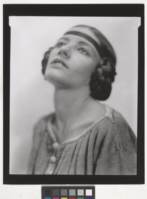 A black-and-white portrait of a White woman, head angled up, with her hair braided into buns on the sides of her head.