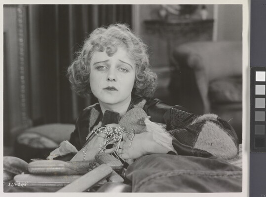A black-and-white photograph of a White woman holding jewelry to her chest as she sadly gazes into the distance.