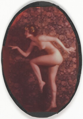 A faded color oval-shaped photograph of a nude, fair-skinned women posed as if in the middle of a dance, with one leg bent, arms out, and yellow flowers in her hair.
