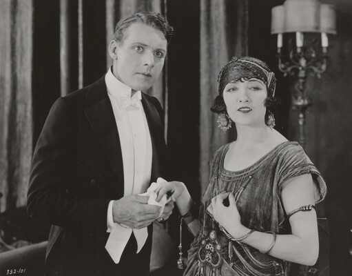 A black-and-white photograph of a White woman and a White man, both elegantly dressed and looking at something in the distance.