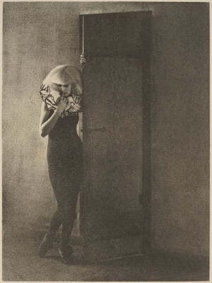 A black-and-white soft focus photograph of a White woman wearing a ruffled collar and black body suit leaning into an open door.