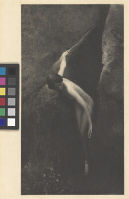 A sepia-toned photograph of a nude woman emerging from between two large boulders.