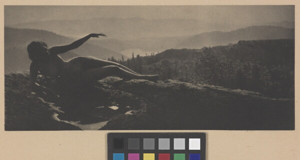 A sepia-toned photograph of a nude woman in shadow lying on a hilltop with cascading hills behind her.