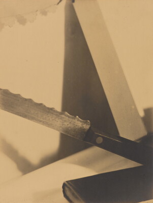 A sepia-toned, close-cropped, abstract photograph of several objects leaning at different angles, including a book and serrated knife.