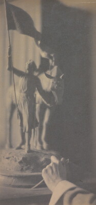 A vertically-oriented black-and-white photograph of a hand reaching toward a sculpture of a girl holding a flag in one hand and a horse's rein in the other.