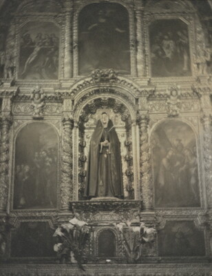 A black-and-white photograph of a sculpture of the Virgin Mary on an altar surrounded by paintings and decorative woodwork.