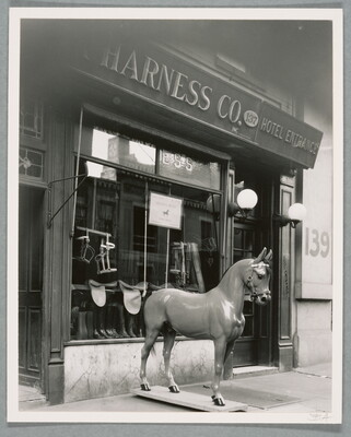 A black-and-white photograph of a storefront with a horse statue on the sidewalk in front of a display window.