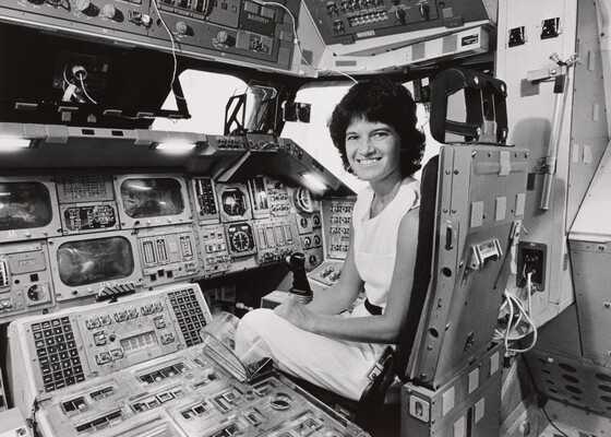 A black-and-white photograph of a White woman with short dark hair sitting in the cockpit of a space shuttle.