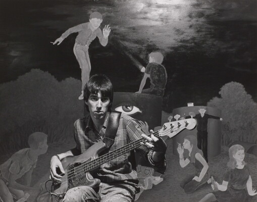 A black-and-white photograph of a young White man playing an electric bass guitar in front of a mural of people smoking and drinking.