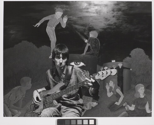 A black-and-white photograph of a young White man playing an electric guitar in front of a mural of people smoking and drinking.