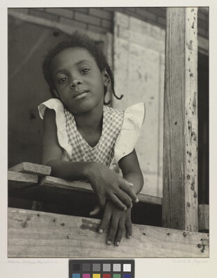 A black-and-white photograph of a young Black girl in a gingham top leaning out of a window.