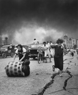 A black-and-white photograph of Asian people running, driving, or riding bicycles from billowing smoke rising behind them.
