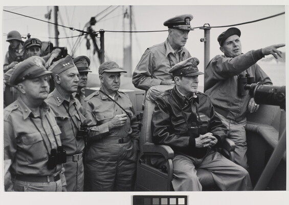 A black-and-white photograph of White men in military uniforms, binoculars hanging around their necks, looking in the direction one of the men is pointing.
