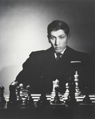 A black-and-white portrait photograph of a White man sitting and studying a chess board.