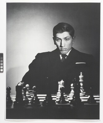 A black-and-white portrait photograph of a White man sitting and studying a chess board.