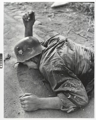 A black-and-white photograph of a deceased, White soldier laying facedown on a road.