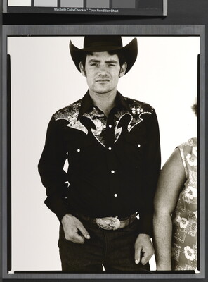 A black-and-white portrait photograph of a White man wearing a dark button-down shirt with Western details, a large belt buckle, and a cowboy hat.