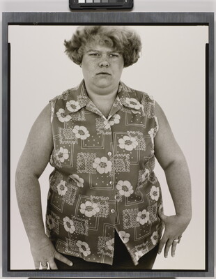 A black-and-white portrait photograph of a White woman with short hair in a sleeveless button-down shirt with a floral pattern.