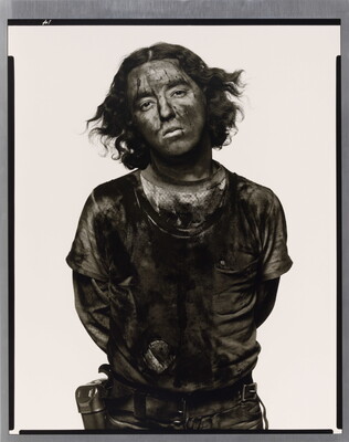A black-and-white portrait photograph of a young man with curly hair covered in dark coal dust.