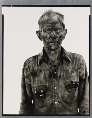 A black-and-white portrait photograph of a man with dirt smudged all over his face and wearing a very dirty button-down shirt.
