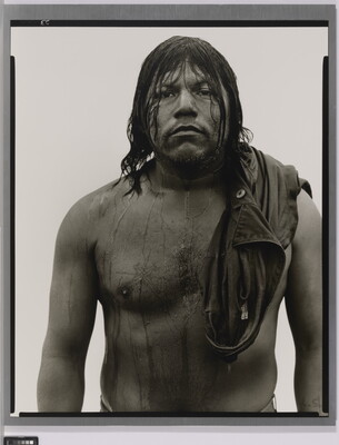A black-and-white portrait photograph of a stocky, dark-skinned man with long, dark wet hair that drips down his shirtless torso.