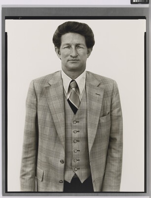 A black-and-white portrait photograph of a dark-haired, White man wearing a three-piece plaid suit with a tie.