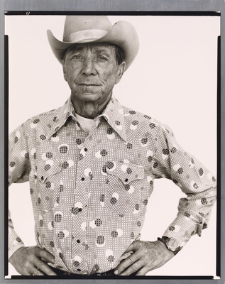 A black-and-white portrait photograph of an older White man wearing a cowboy hat, a button-down shirt, looking straight ahead with hands on hips.