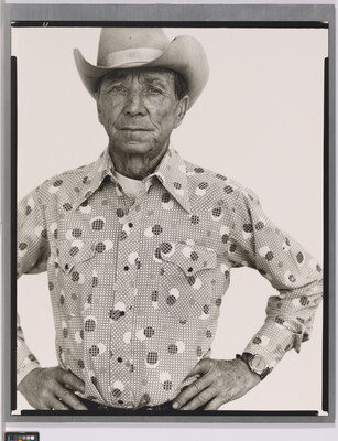A black-and-white portrait photograph of an older White man wearing a cowboy hat, a button-down shirt, looking straight ahead with hands on hips.